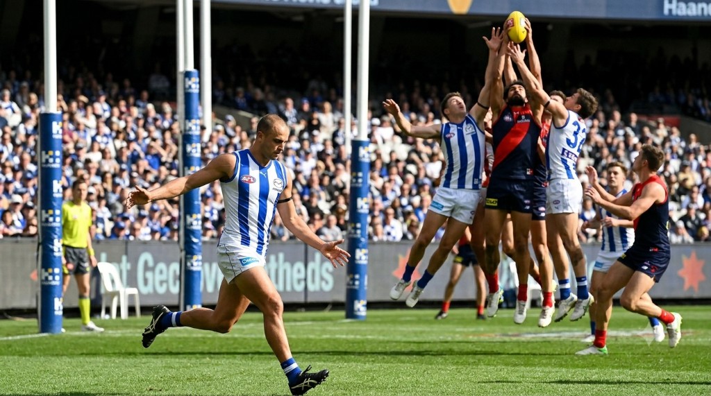 Australian rules football player leaping high to contest the ball in the air in front of spectators.